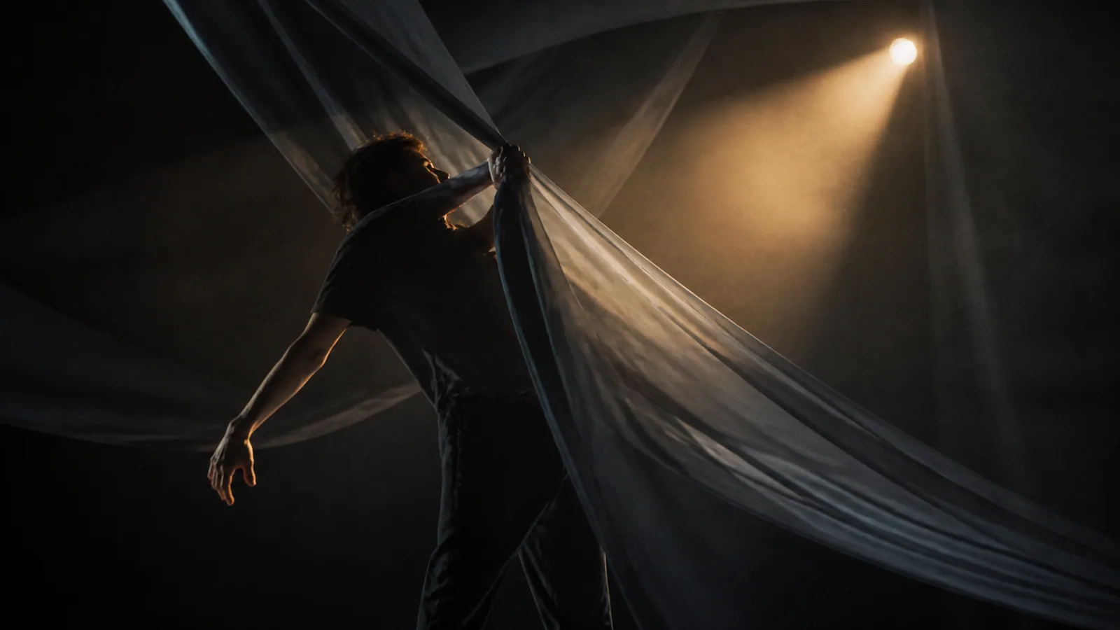 Cinematic still of an anonymous performer moving through translucent fabric and warm stage light